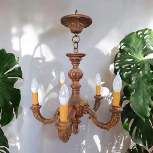 May include: A five-light wooden chandelier with a gold finish. The chandelier has a traditional design with ornate details and candle-style light bulbs.