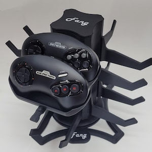 May include: Black Sega Genesis controllers on a black stand with the word "Fang" printed on the front. The stand has six arms to hold the controllers.