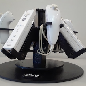 May include: A black rotating stand with a circular base that holds five white Nintendo Wii remotes. The stand has a black label with the word "Fang" on it.