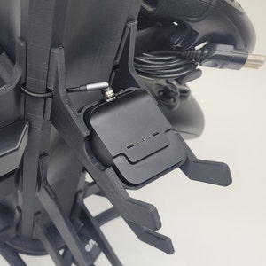 Könnte beinhalten: Ein schwarzer Plastikständer mit einer schwarzen Ladestation an der Seite. Der Ständer hat mehrere Steckplätze zum Aufbewahren von verschiedenen Gaming-Zubehör.