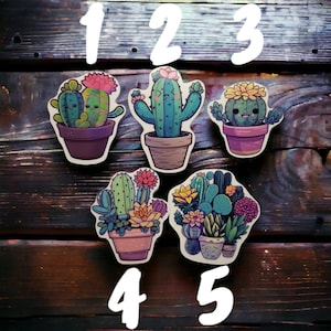 Peut inclure: Cinq autocollants de cactus colorés avec des designs différents. Les autocollants sont numérotés de 1 à 5. Les autocollants sont sur un fond en bois.