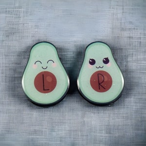 May include: Two green avocado-shaped pins with cute faces. The left pin has a red circle with the letter "L" inside. The right pin has a red circle with the letter "R" inside.
