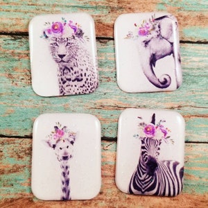 May include: Four square white coasters with a glittery finish. Each coaster features a different animal with a floral crown: a leopard, an elephant, a giraffe, and a zebra.