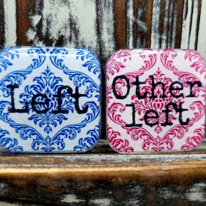 May include: Two square ceramic tiles with a white background and a blue and pink damask pattern. The tile on the left says "Left" in black lettering. The tile on the right says "Other Left" in black lettering.