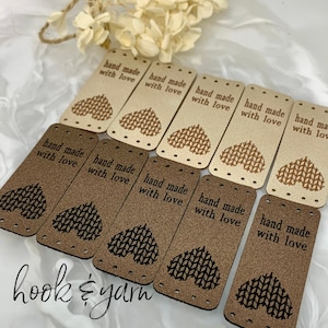 May include: Ten brown leather labels with a heart-shaped knitted pattern and the text "hand made with love" printed on each. The labels are arranged in two rows, with the top row containing five labels and the bottom row containing five labels. The labels are on a white surface.