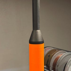 May include: A black and orange 3D printed filament guide with a rounded top. The guide is sitting on top of a 3D printer.