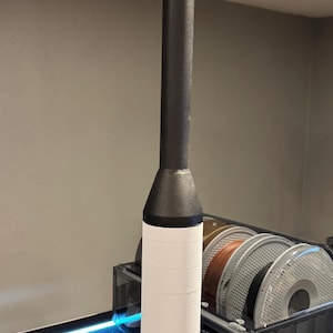 Puede incluir: Un objeto impreso en 3D en blanco y negro con una parte superior redondeada y una base cilíndrica. El objeto está colocado encima de una impresora 3D.