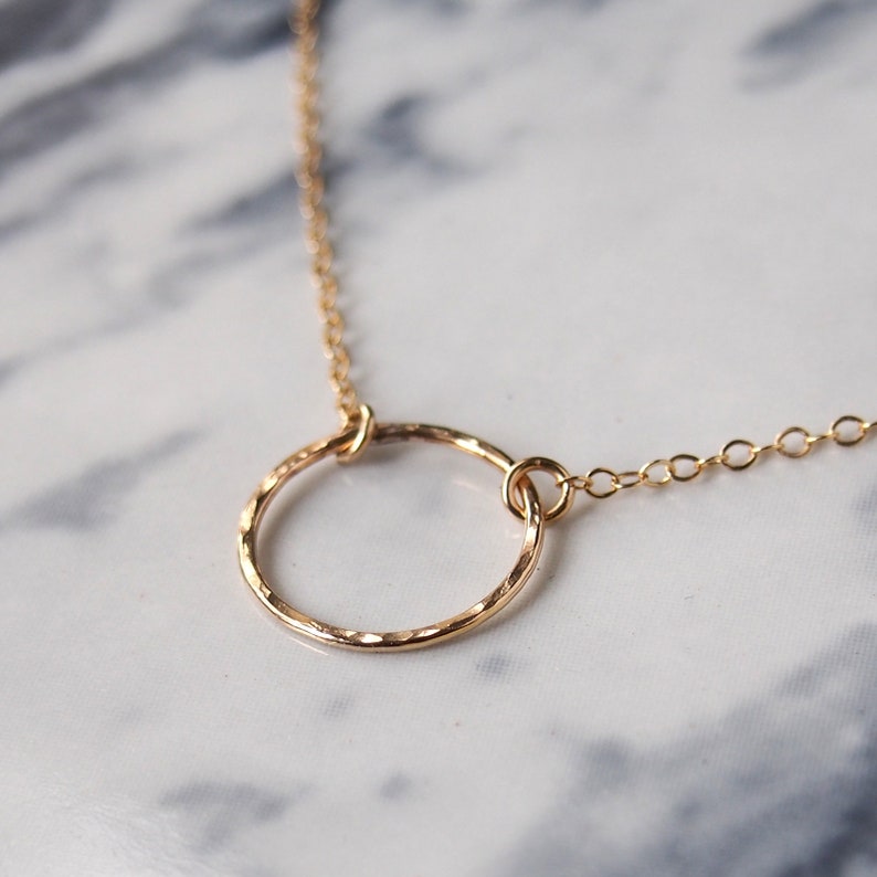 K&ouml;nnte beinhalten: Eine goldene Halskette mit einem geh&auml;mmerten Kreisanh&auml;nger. Die Kette ist zart und der Kreis ist schlicht und elegant.