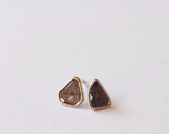 May include: A pair of silver stud earrings with a rough, irregular shaped black stone set in each.