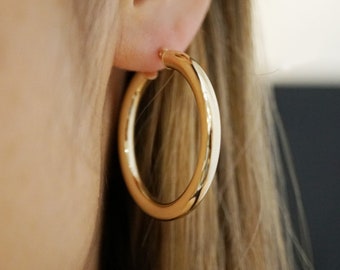May include: Gold hoop earrings with a smooth, polished finish. The earrings are large and circular, with a diameter of approximately 2 inches.