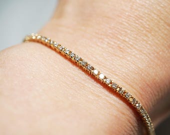 May include: A delicate gold bracelet with numerous small, sparkling diamonds set closely together. The bracelet is a warm gold color and is shown on a wrist, highlighting the jewelry's elegant design. The diamonds catch the light, creating a brilliant display.