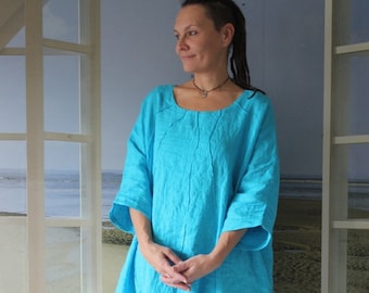 Op de afbeelding: Een turquoise linnen jurk met een ronde halslijn en elleboogmouwen. De jurk heeft een losse, vloeiende silhouet en valt tot op de enkels. Het model staat voor een raam met een strandscène.