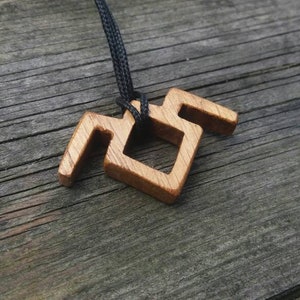 Puede incluir: Un collar con un colgante de madera con un diseño geométrico. El colgante está hecho de madera marrón claro y tiene un cordón negro.