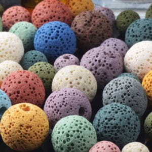 May include: A selection of spherical, porous stones in a range of colours, such as red, blue, green, yellow, and purple. The stones have a textured surface with many small holes, creating a unique visual appeal. The arrangement suggests a decorative or natural theme.