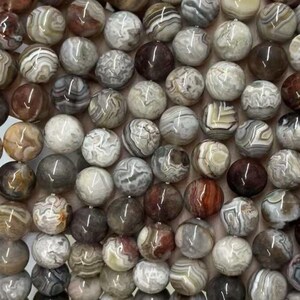 May include: A close-up of a collection of round gemstone beads in shades of brown, grey, and white. The beads display unique patterns and textures, offering a natural aesthetic. Suitable for jewellery making and craft projects.