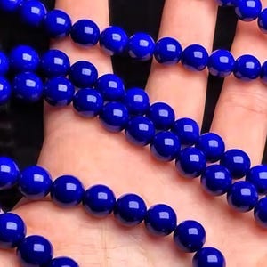 May include: Close-up of strands of deep blue, glossy beads. The beads are round and evenly sized, creating a smooth, reflective surface. The image highlights the color and texture of the beads, suggesting they are for jewelry making or crafting.
