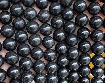 May include: Close-up of a collection of glossy, black, spherical beads. The beads are arranged closely together, filling the frame. The smooth, reflective surfaces catch the light, creating highlights. The beads appear to be made of a polished material.
