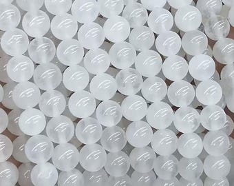 Puede incluir: Primer plano de un collar de cuentas blancas y redondas. Las cuentas son de tamaño uniforme y parecen estar hechas de un material translúcido. Las cuentas están ensartadas, creando un patrón de esferas repetidas.