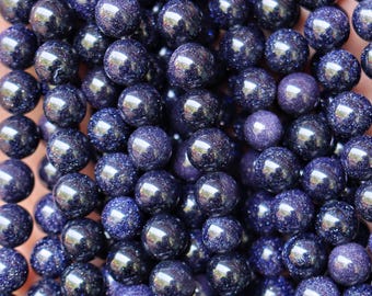 May include: Close-up of a collection of dark blue aventurine gemstone beads. The beads are round, polished, and have a sparkling, glittery appearance. The beads are strung together, ready for jewelry making.