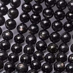 Puede incluir: Primer plano de una colección de cuentas negras pulidas y redondas. Las cuentas tienen una superficie brillante y reflectante, con sutiles variaciones de color y textura. Las cuentas están dispuestas en un patrón de cuadrícula, llenando el marco.