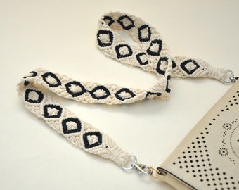 May include: A white and black crocheted bag strap with a diamond pattern. The strap is attached to a light brown leather bag with a cut-out design.