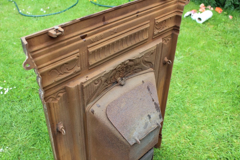 Pu&ograve; includere: Un camino in ghisa vintage con dettagli intricati e un design decorativo. Il camino &egrave; di colore marrone ruggine e ha il numero "N189 122" inciso sulla parte superiore.