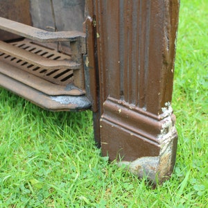 Pu&ograve; includere: Primo piano di un camino in ghisa marrone con una griglia e una base decorativa. Il camino &egrave; appoggiato su un letto di erba verde.