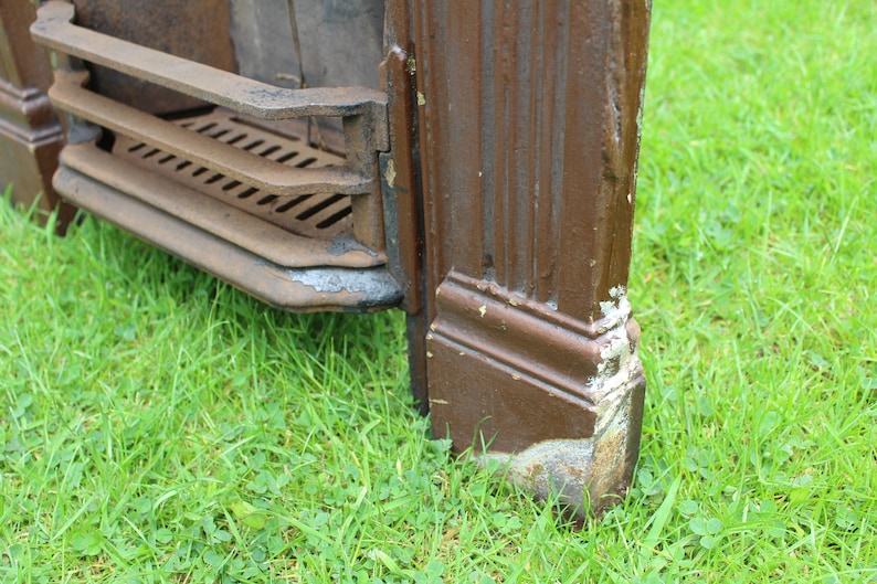 Pu&ograve; includere: Primo piano di un camino in ghisa marrone con una griglia e una base decorativa. Il camino &egrave; appoggiato su un letto di erba verde.