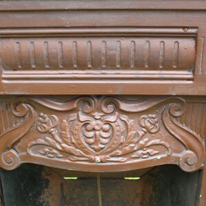 Pu&ograve; includere: Un camino in ghisa marrone con intricati dettagli floreali e a volute. Il camino ha una parte superiore decorativa rialzata con un design centrale a forma di cuore.