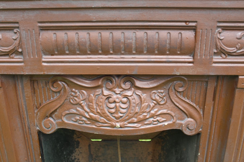 Pu&ograve; includere: Un camino in ghisa marrone con intricati dettagli floreali e a volute. Il camino ha una parte superiore decorativa rialzata con un design centrale a forma di cuore.