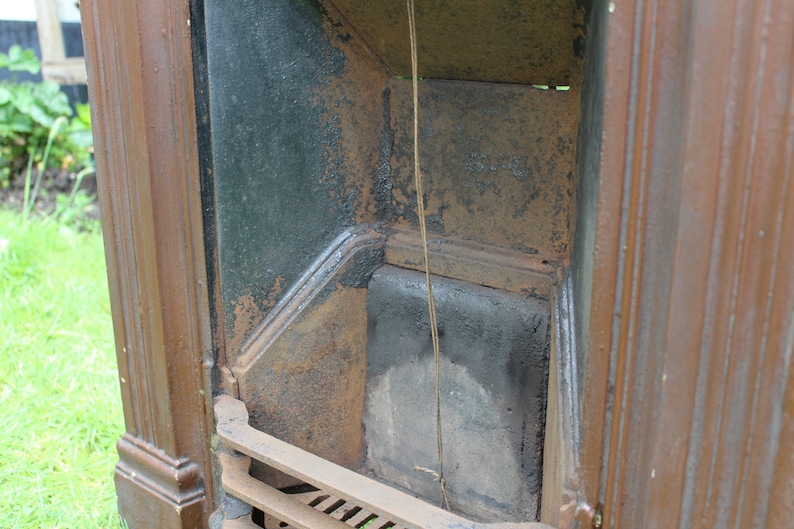 Pu&ograve; includere: Primo piano dell'interno di un camino in ghisa. Il camino &egrave; dipinto di nero e presenta una patina rugginosa. Il focolare &egrave; vuoto e la griglia &egrave; visibile.
