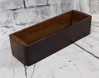 Può includere: Una scatola di legno rettangolare con una macchia marrone scuro. La scatola è vuota e ha una finitura liscia e lucida.