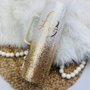May include: A gold and white glitter tumbler with a handle. The tumbler has the name "Liz" written on it in gold lettering.
