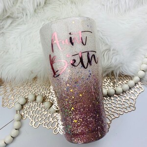 May include: A white and pink glitter tumbler with a rose gold vinyl design that says "Aunt Beth".