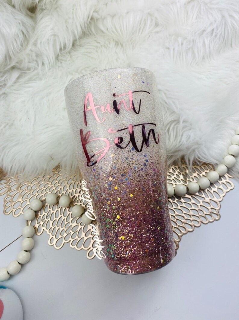 May include: A white and pink glitter tumbler with a rose gold vinyl design that says "Aunt Beth".