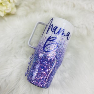 May include: A white and purple glitter tumbler with a handle. The tumbler has the text "Mama B" written on it in purple.