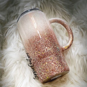 May include: A white and rose gold glitter ombre tumbler with a black lid and handle. The tumbler has the text "Sippie Couture" on the side.