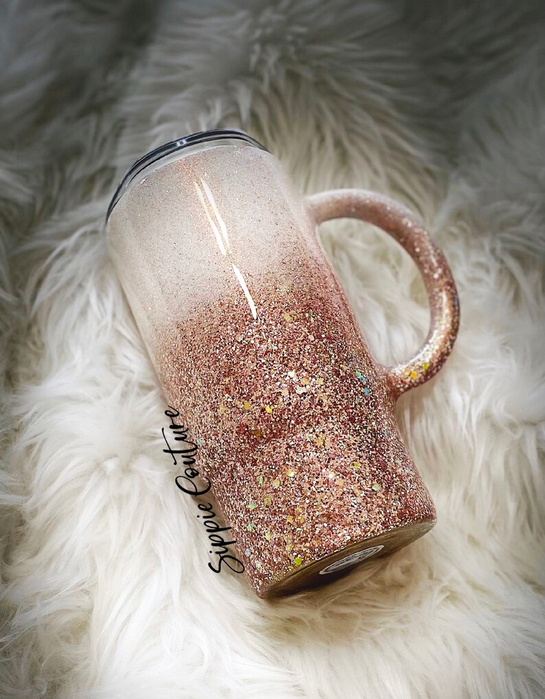 May include: A white and rose gold glitter ombre tumbler with a black lid and handle. The tumbler has the text "Sippie Couture" on the side.