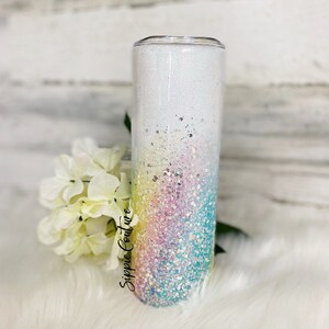 May include: A white tumbler with a rainbow glitter ombre design. The tumbler has a clear lid and is decorated with the text "Sippie Couture".
