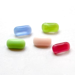 Könnte beinhalten: Fünf kleine, bunte, ovale Glasperlen. Die Perlen sind hellblau, hellgrün, rosa und rot.