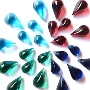 Peut inclure: Collection de perles en verre en forme de goutte d'eau, de couleurs bleu, vert et rouge, disposées sur un fond blanc. Les perles varient en taille et en intensité de couleur, créant un affichage visuellement attrayant. Idéal pour les projets de bijoux ou d'artisanat.