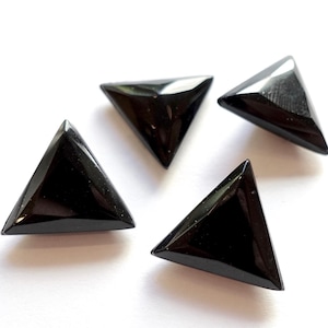 Può includere: Quattro cabochon di pietra preziosa triangolari neri su uno sfondo bianco.