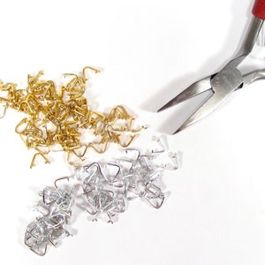 May include: A pair of silver-toned pliers with red handles, next to a pile of gold and silver jump rings. The jump rings are used for jewelry making.
