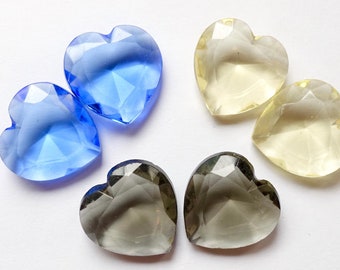 May include: Five heart-shaped glass embellishments in blue, grey, and yellow. The embellishments are faceted and have a shiny finish.