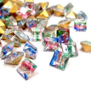 May include: Assortment of colourful, iridescent, square-shaped glass rhinestones. The rhinestones have a variety of colours, including blue, green, pink, and gold.