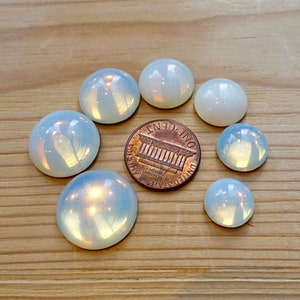 Könnte beinhalten: Sieben irisierende weiße Opal-Cabochons in verschiedenen Größen, angeordnet in einem Kreis um einen Kupferpfennig mit der Aufschrift "ONE CENT".
