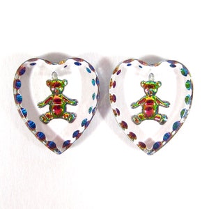 May include: Two clear heart-shaped glass beads with a rainbow iridescent finish. Each bead features a small, metallic teddy bear inside.