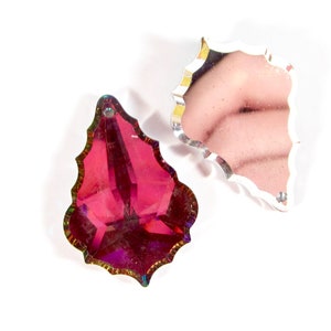 Puede incluir: Dos colgantes de prisma de cristal iridiscente en forma de hoja. El colgante de la izquierda es de color rojo intenso, mientras que el colgante de la derecha es transparente.