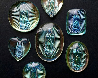 May include: Eight iridescent glass charms featuring a depiction of the Virgin Mary. The charms are in various shapes, including hearts, ovals, and rectangles. The glass is clear with a rainbow sheen.