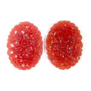 May include: Two red carved oval-shaped pendants with intricate floral designs.